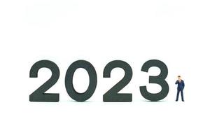 2023 año nuevo y concepto de planificación empresarial. Primer plano de figuras en miniatura de empresario de pie con bloque numérico de madera sobre fondo blanco. foto