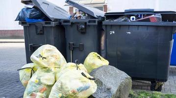 Overflowing plastic garbage containers and waste package lie on a city street. photo