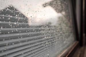 Raindrops on the glass of the window, which reflects the house and the cloudy sky, outdoors. photo