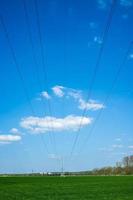 High metal electricity pylons with power lines that pass over an agricultural field, against the backdrop of a blue sky and clouds. photo