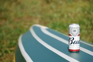 SUMY, UKRAINE - AUGUST 01, 2022 Can of Budweiser Lager Alcohol Beer on overturned kayak boat outdoors. Budweiser is a Brand from Anheuser-Busch Inbev photo