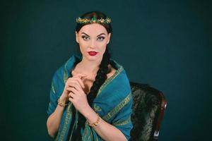 Portrait of young beautiful brunette in Indian style with wreath and braid in a blue scarf and gold bracelets on dark background photo