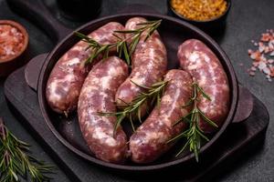 Raw pork sausages grill with spices and herbs on a dark concrete table photo