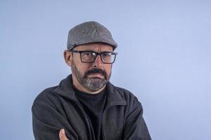 Portrait of 60 years old bearded man on blue background with hat and glasses photo