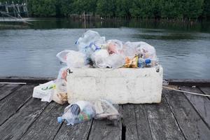 selective focus to trash bin of various types of leftover food and plastic drink bottles on wooden bridge over river photo