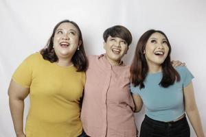 A portrait of three friends looks excited pointing at the copy space upside them, isolated by white background photo