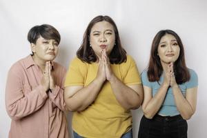 Three friends in casual clothes waiting for special moment, begging in prayer gesture together isolated on white color background studio. photo