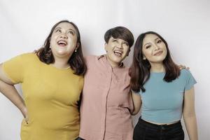 A portrait of three friends looks excited pointing at the copy space upside them, isolated by white background photo