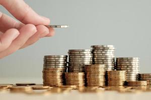 Hand hold a money coin for put on stack of coins. Financial and business, saving money, loan, tax, interest rate, plan for investment in the future concept. photo