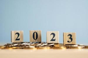 2023 feliz año nuevo. negocio y ahorro de dinero, crecimiento financiero, aumento de la tasa de interés, inflación, precio de venta y concepto de aumento de impuestos. bloques de madera número 2023 en monedas. foto