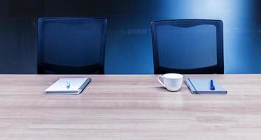 Coffee cup and notebook on table with two black armchairs in meeting room photo