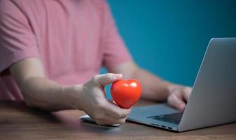 Man hand holding Red heart and using laptop computer,  giving, donation, insurance, love chat online dating concept. photo