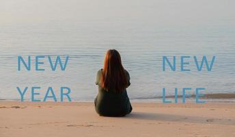 New year new life quote on the image of woman sitting on the sand beach. photo