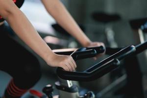 Crop picture of close up hand sportswoman exercising on a bicycle in the gym, determination to cardio lose weight, makes her healthy. exercise bike woman fitness sport concept. photo