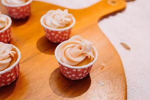 pastelitos gourmet con glaseado de crema de mantequilla blanca y chispas sobre fondo de madera foto