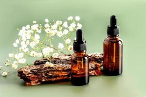 two bottles with a dropper with a serum for skin care of the face against the background of the bark of the tree and flowers.