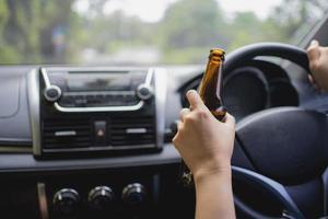 A faceless woman is drinking a bottle of beer while driving a car. Drunk driving concept photo