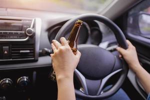 Concept of driving intoxicated, hand holding alcohol while driving. photo