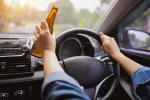 un conductor que sostiene una botella de alcohol mientras conduce. concepto de conducir ebrio. foto