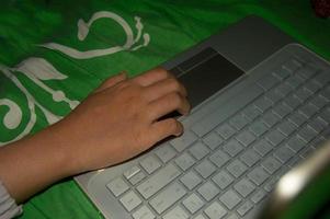 la mano de una mujer jugando en una computadora portátil. una mujer que trabaja con una computadora portátil en la cama foto