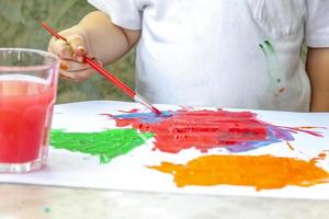 The child draws a bright picture. Large strokes of paint on paper. photo