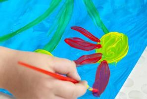 The child draws a bright picture. Large strokes of paint on paper. photo