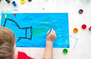 The child draws a bright picture. Large strokes of paint on paper. photo