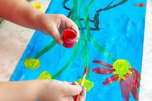 The child draws a bright picture. Large strokes of paint on paper. photo