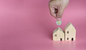 una mano humana puso una moneda en la casa modelo. ideas para ahorrar dinero para comprar una nueva casa y préstamos para planificar futuras inversiones inmobiliarias. foto