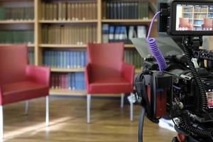 Two empty chairs in a TV studio with book panel in the background and camera in the foreground photo