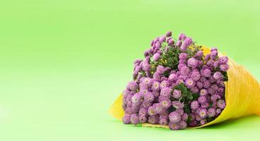 Bouquet of small lilac chrysanthemums in yellow paper on green background. Congratulation, birthday gift, international women's, mother's day. Copy space photo