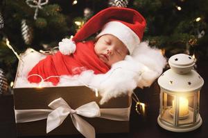 Cute newborn baby wearing Santa Claus hat is sleeping in the Christmas gift box photo