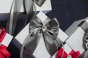 Many gifts. The gift box is white with a red and gray beautiful bow. Gift on a dark background. Holidays and surprises. Satin bows with rhinestones. photo