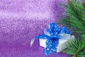 regalo de navidad blanco con hermoso lazo azul. regalo bajo el árbol de Navidad sobre un fondo morado. foto