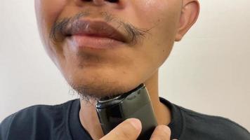 a man shaves his own beard using an electric shaver. men care
