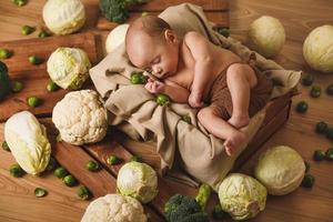 Little baby is lying in the box with a lot of different cabbages photo