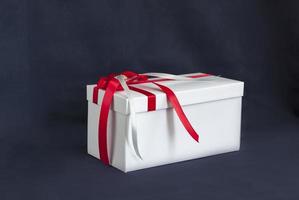 The gift box is white with a beautiful red bow. Gift on a dark background. Holidays and surprises. Satin bows with rhinestones. photo