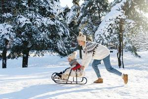 Mother and her cute little son having on a sledding hill during sunny winter day photo