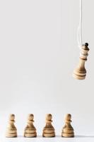 Wooden chess queen hanging on a white rope with pawns standing below. photo