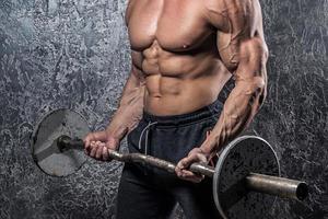 Bodybuilder man with barbell against concrete wall photo