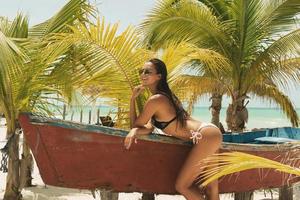 Beautiful woman wearing bikini and sunglasses beside a old boat photo