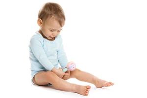 Little boy in romper sitting and playing with plastic rattle. photo