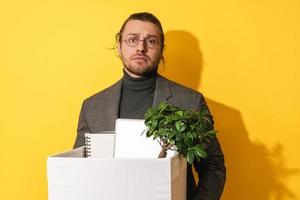 Upset man holding box with personal items after job resignation against yellow background photo