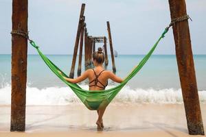 Woman is relaxing in the hammock hanging on old beams from the broken pier photo