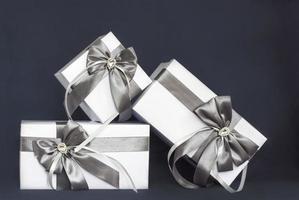 The gift box is white with a beautiful gray bow. Gift on a dark background. Holidays and surprises. Satin bows with rhinestones. photo