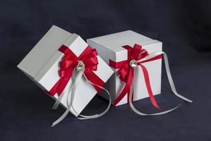 muchos regalos. la caja de regalo es blanca con un hermoso lazo rojo y gris. regalo sobre un fondo oscuro. vacaciones y sorpresas. lazos de raso con pedrería. foto