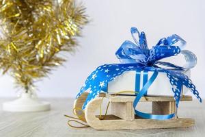 A Christmas gift with a large blue bow is lying on a wooden sleigh. Happy New year and merry Christmas. photo