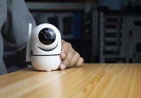 White ip camera lies on wooden floor, man using ip camera photo