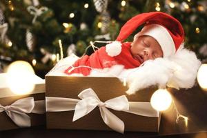 Cute newborn baby wearing Santa Claus hat is sleeping in the Christmas gift box photo