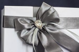 The gift box is white with a beautiful gray bow. Gift on a dark background. Holidays and surprises. Satin bows with rhinestones. photo